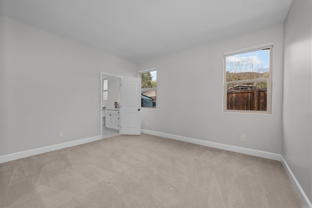 empty room with a healthy amount of sunlight, baseboards, and light colored carpet