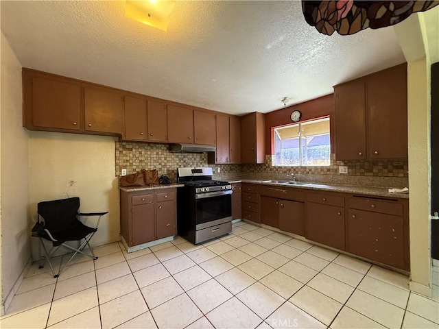 kitchen featuring light tile patterned floors, backsplash, a sink, gas range, and under cabinet range hood