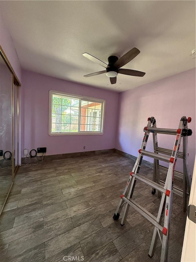 exercise area with wood finished floors, a ceiling fan, and baseboards