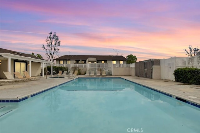 pool at dusk with a patio, fence, and a community pool