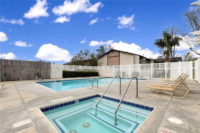 community pool with a patio area, fence, and a hot tub