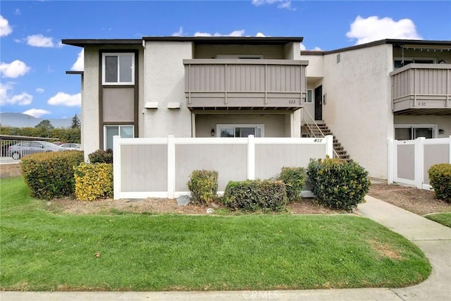 view of front of house featuring stucco siding, fence, a balcony, a front lawn, and stairs