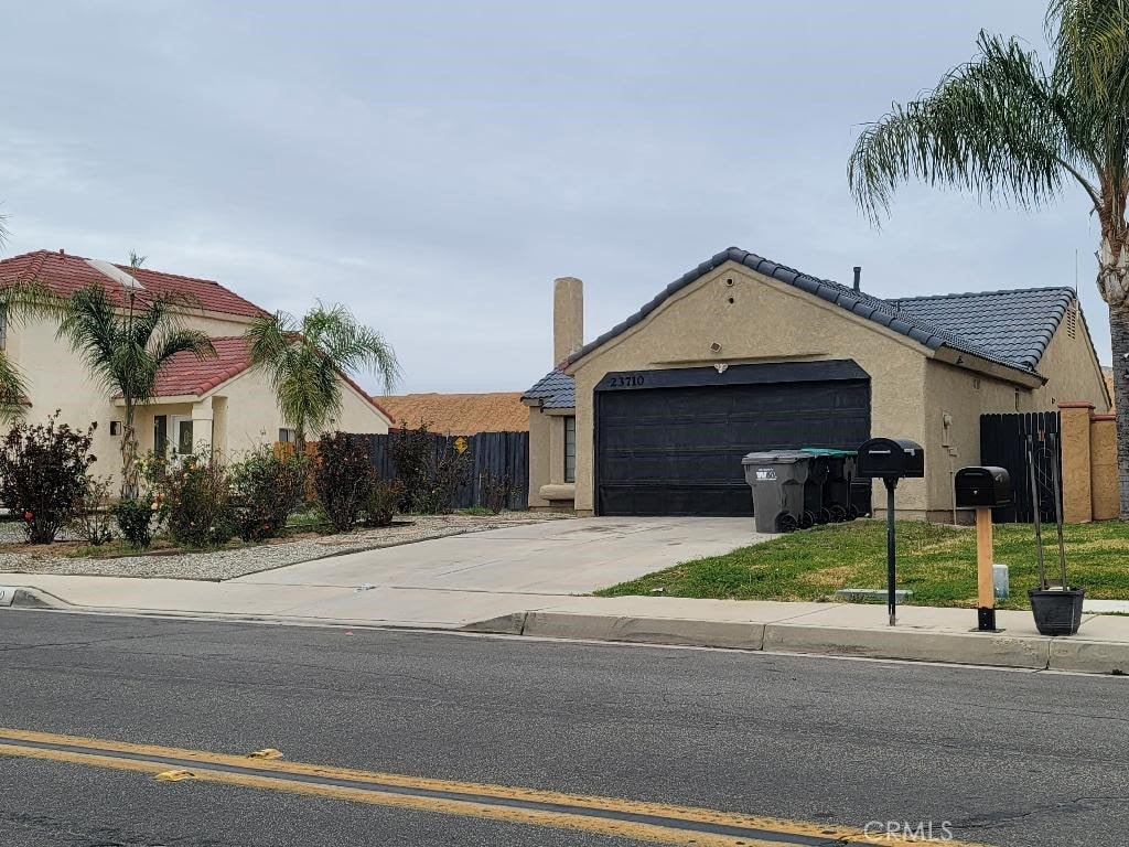 view of front of house featuring an attached garage, fence, driveway, a tiled roof, and stucco siding