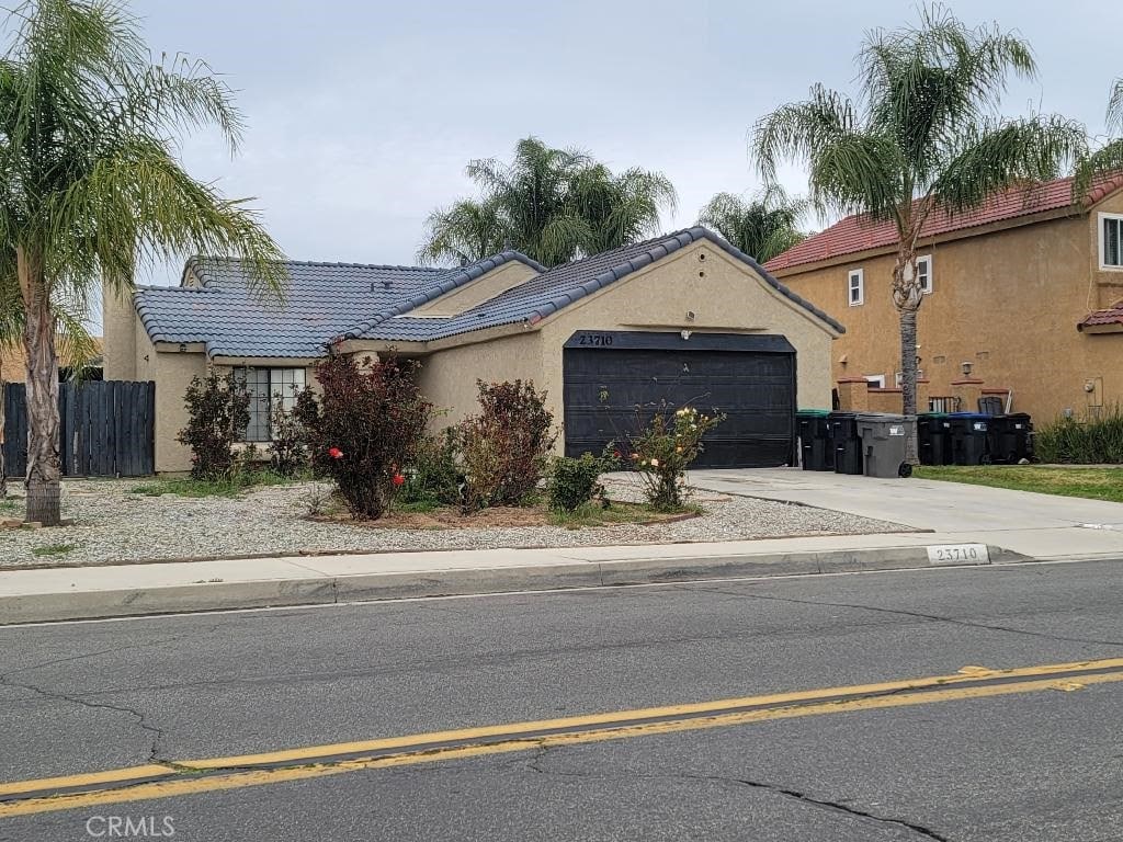 view of front facade with stucco siding, concrete driveway, an attached garage, fence, and a tiled roof