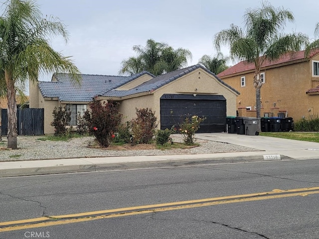 view of front facade with stucco siding, concrete driveway, an attached garage, fence, and a tiled roof