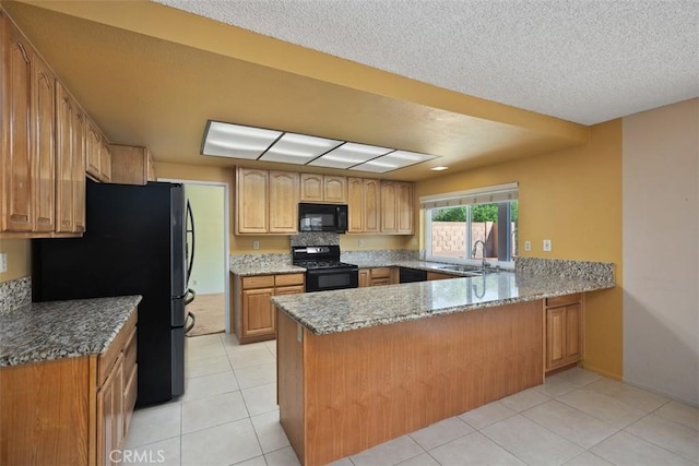 kitchen featuring black appliances, light stone counters, a peninsula, and a sink