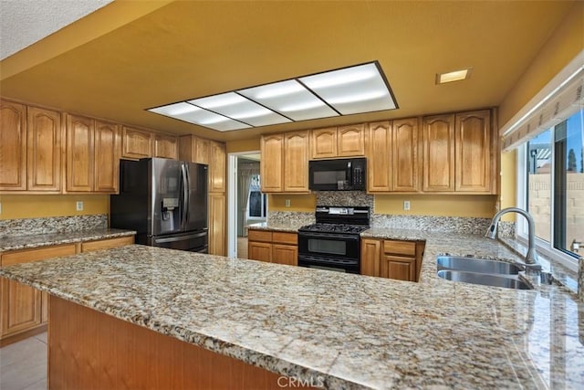 kitchen featuring a sink, light stone countertops, black appliances, and a peninsula