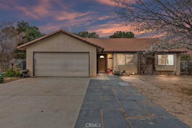 ranch-style house with a garage, a tile roof, concrete driveway, and stucco siding