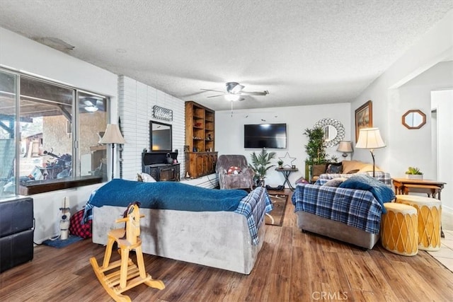 living area featuring a textured ceiling, a wood stove, wood finished floors, and a ceiling fan