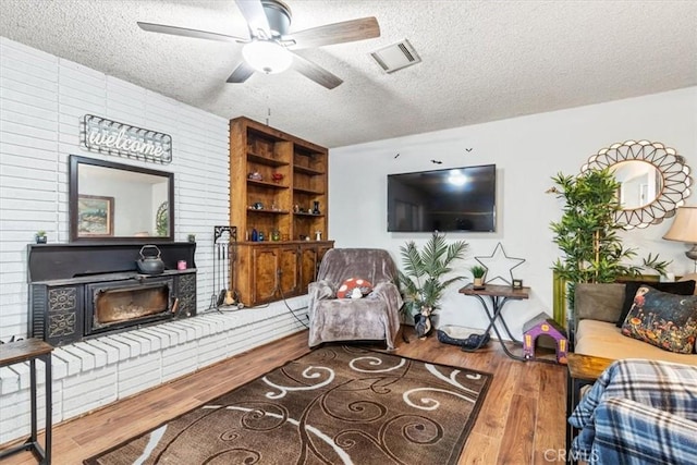 living room featuring visible vents, a ceiling fan, a glass covered fireplace, wood finished floors, and a textured ceiling