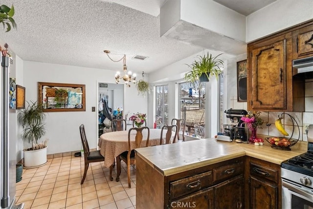 kitchen with a textured ceiling, light tile patterned flooring, a peninsula, light countertops, and stainless steel range with gas stovetop