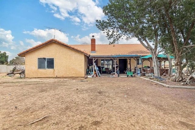 back of house with a chimney, a patio, a tiled roof, and stucco siding