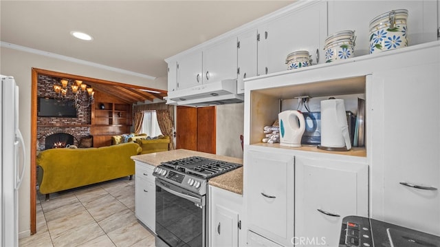 kitchen with under cabinet range hood, a brick fireplace, stainless steel range with gas cooktop, freestanding refrigerator, and crown molding