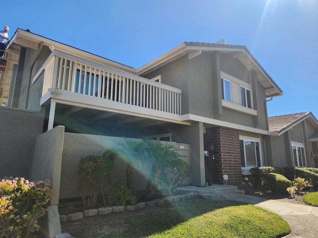 view of front of house featuring a balcony, brick siding, and stucco siding