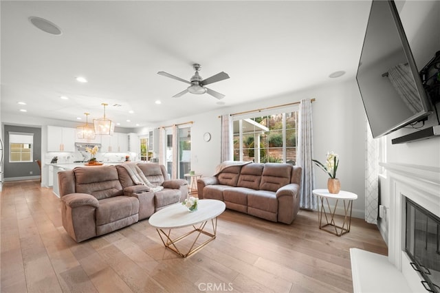 living room featuring a wealth of natural light, a glass covered fireplace, light wood-style flooring, and recessed lighting