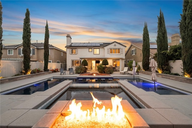 back of house at dusk with a fire pit, solar panels, a standing seam roof, and a fenced backyard