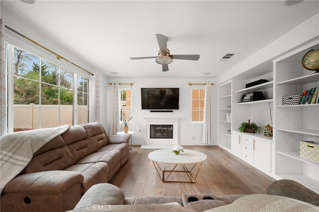 living area with a ceiling fan, a glass covered fireplace, wood-type flooring, and visible vents