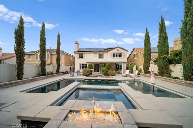 rear view of house featuring a fire pit, a patio area, a fenced backyard, and roof mounted solar panels