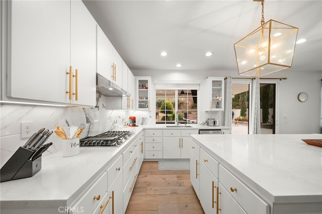 kitchen with light wood-style flooring, under cabinet range hood, white cabinets, tasteful backsplash, and stainless steel gas stovetop