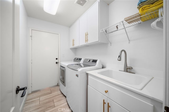 washroom featuring wood finish floors, visible vents, cabinet space, a sink, and washer and dryer