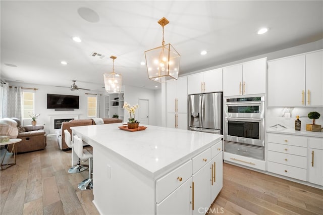 kitchen with visible vents, light wood-style floors, appliances with stainless steel finishes, a warming drawer, and a glass covered fireplace