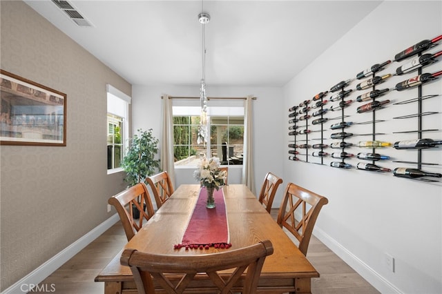 dining area with wallpapered walls, wood finished floors, visible vents, and baseboards