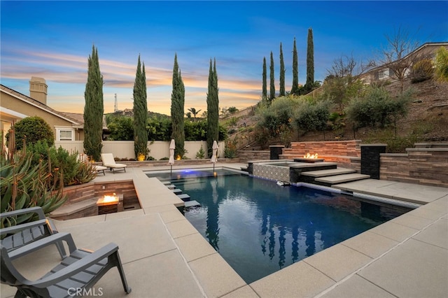 pool at dusk featuring a pool with connected hot tub, a fenced backyard, a patio, and a fire pit