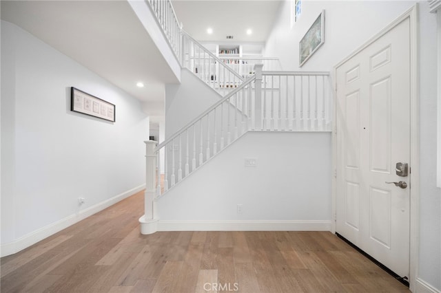 stairway featuring a towering ceiling, baseboards, wood finished floors, and recessed lighting