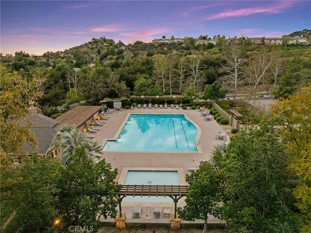 pool at dusk with a patio area and a community pool