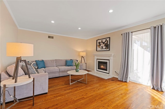 living area with recessed lighting, a high end fireplace, visible vents, light wood-type flooring, and crown molding