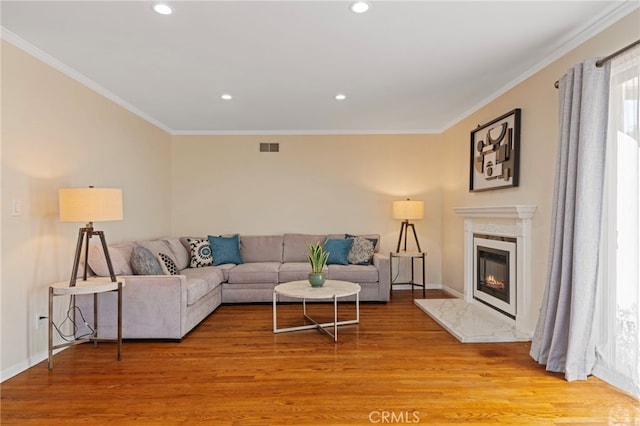 living area featuring ornamental molding, a premium fireplace, light wood-style flooring, and recessed lighting