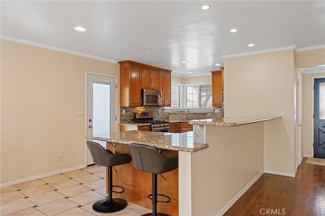 kitchen with appliances with stainless steel finishes, a peninsula, light stone countertops, crown molding, and backsplash