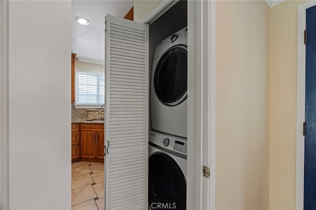 laundry area featuring light tile patterned floors, laundry area, a sink, stacked washer / drying machine, and ornamental molding