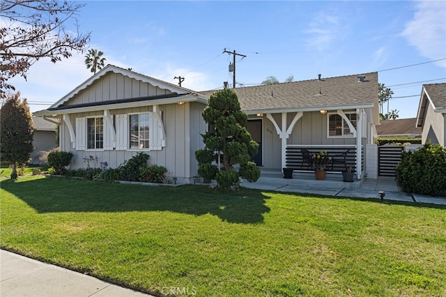 view of front of home with covered porch, roof with shingles, a front lawn, and board and batten siding