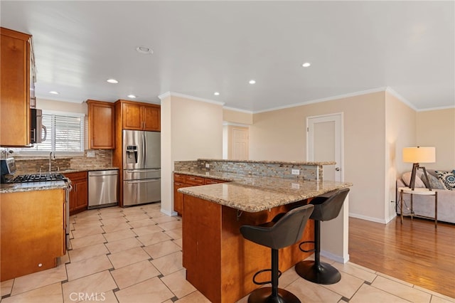 kitchen featuring stainless steel appliances, brown cabinets, crown molding, and a breakfast bar area