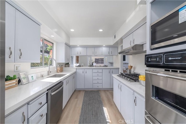 kitchen featuring light wood-style flooring, appliances with stainless steel finishes, light countertops, under cabinet range hood, and a sink