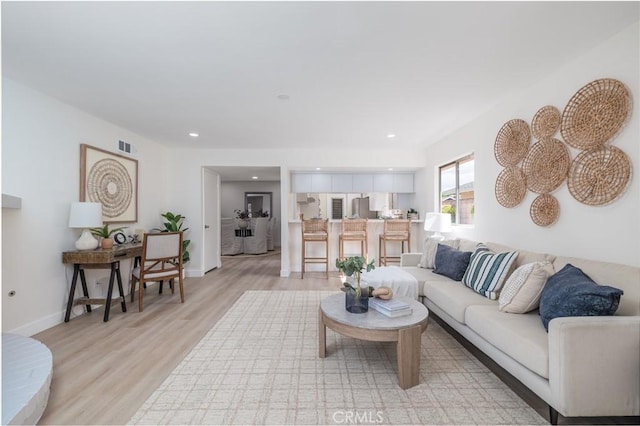 living room with light wood-style flooring, visible vents, baseboards, and recessed lighting