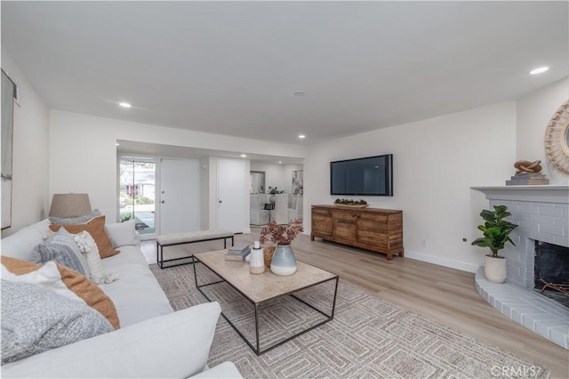 living room with a brick fireplace, light wood-style flooring, baseboards, and recessed lighting