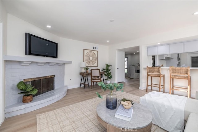 living room featuring a fireplace, recessed lighting, visible vents, light wood-style flooring, and baseboards