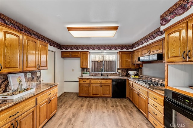 kitchen with black appliances, range hood, brown cabinetry, and a sink