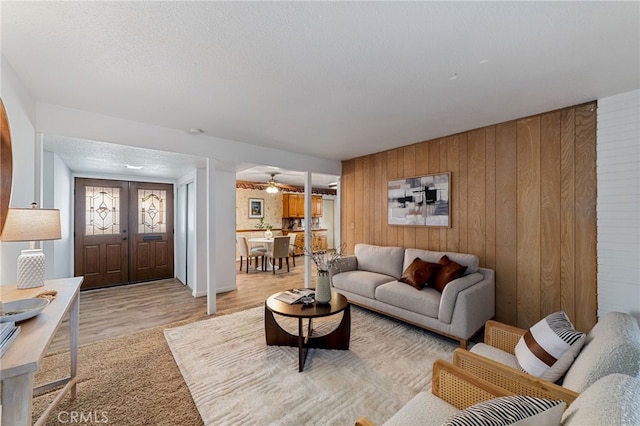 living room with light wood-style floors, wooden walls, a textured ceiling, and french doors