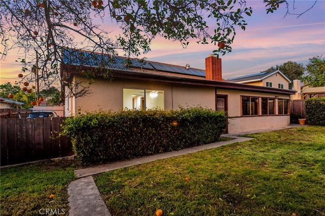 rear view of property featuring roof mounted solar panels, fence, a lawn, and stucco siding