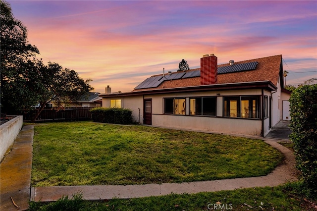 back of property at dusk featuring fence, a sunroom, a lawn, stucco siding, and a chimney