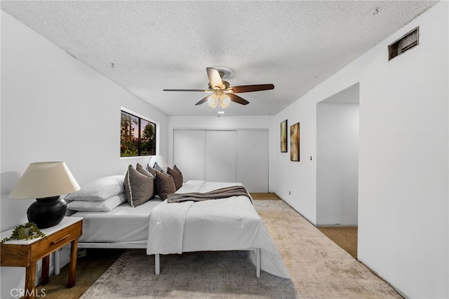 bedroom with carpet floors, a closet, visible vents, a ceiling fan, and a textured ceiling