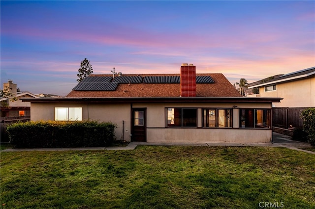 rear view of house featuring a lawn, a chimney, fence, and stucco siding