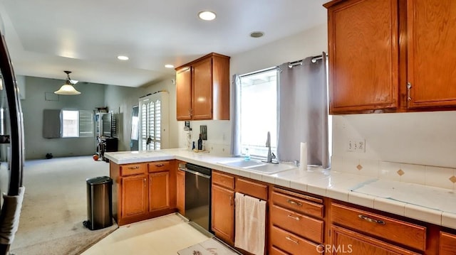 kitchen featuring brown cabinetry, light countertops, dishwasher, and a sink