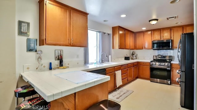 kitchen with visible vents, brown cabinetry, a peninsula, stainless steel appliances, and a sink