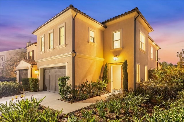 mediterranean / spanish-style home with a tiled roof, concrete driveway, an attached garage, and stucco siding