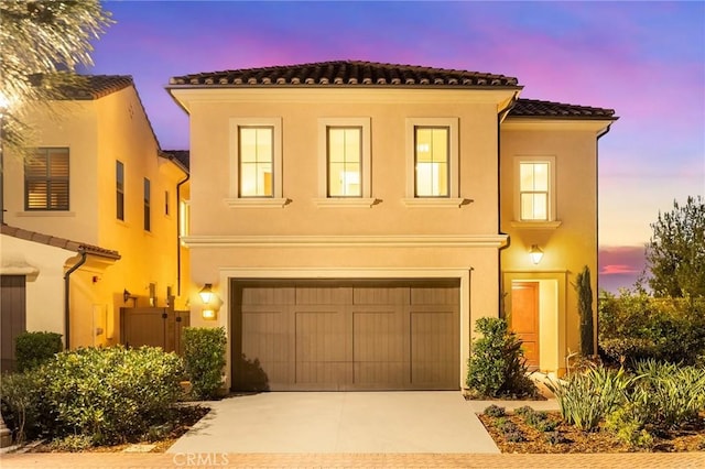 mediterranean / spanish-style house featuring a garage, a tiled roof, concrete driveway, and stucco siding