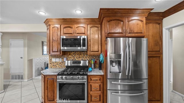 kitchen featuring baseboards, decorative backsplash, brown cabinetry, and appliances with stainless steel finishes